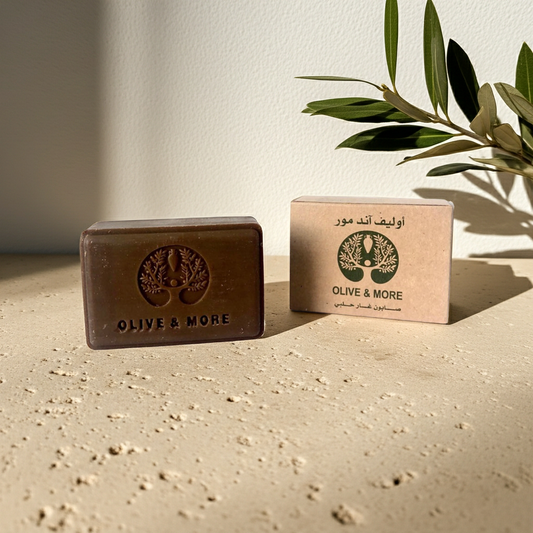 Aleppo Laurel Soap — bar shown beside its dark brown box on a textured beige surface, with an olive branch and green leaves