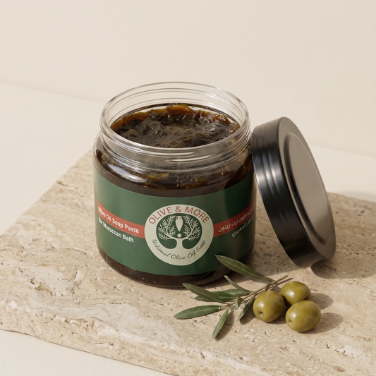 Olive Oil Soap Paste for Moroccan Bath — open glass jar with its lid beside it on a textured stone slab, with an olive branch and olives