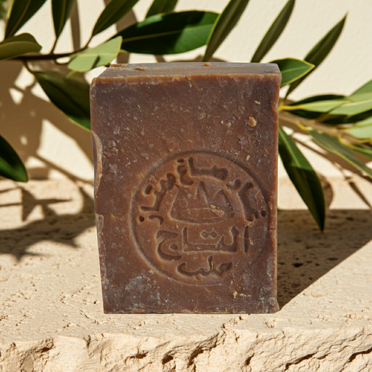Aleppo Laurel Soap by Al Taj — tan bar of Aleppo soap standing upright on a stone surface, with leaves