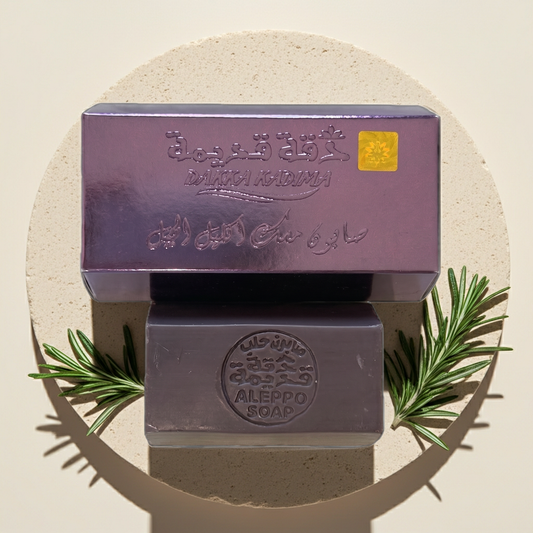 Rosemary Musk Aleppo Soap by Dakka Kadima — two bars stacked on a stone slab, the top one in its purple box, with rosemary sprigs