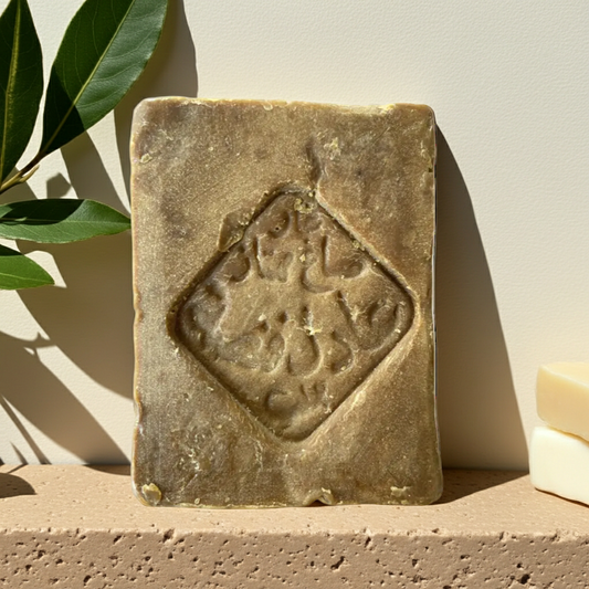 Original Aleppo Laurel Soap by Fansa 20% — beige bar of Aleppo soap on a textured beige surface, with green leaves